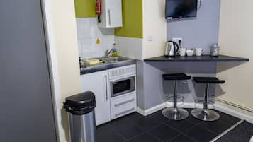 A compact kitchen with a microwave, sink, and two bar stools.