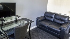 Une pièce avec un bureau en verre, un canapé en cuir noir et un téléviseur.