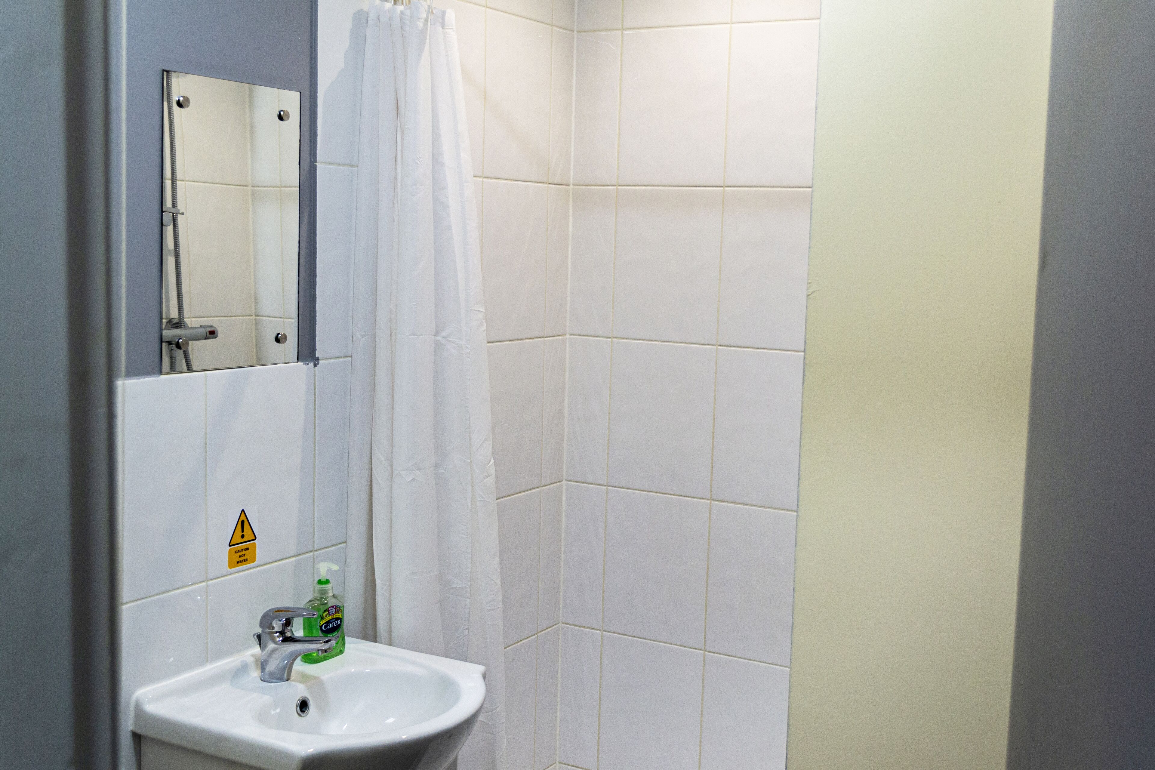 Un bagno con lavandino bianco, uno specchio e una tenda da doccia.