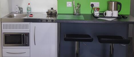 Una cocina moderna con una pared verde de acento, un televisor de pantalla plana, una cafetera y dos taburetes de bar.