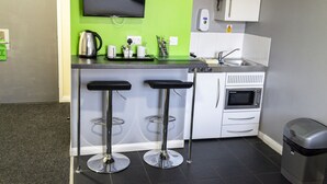 Une cuisine moderne avec un mur d’accent vert, deux tabourets de bar, une machine à café, un four à micro-ondes et un évier.