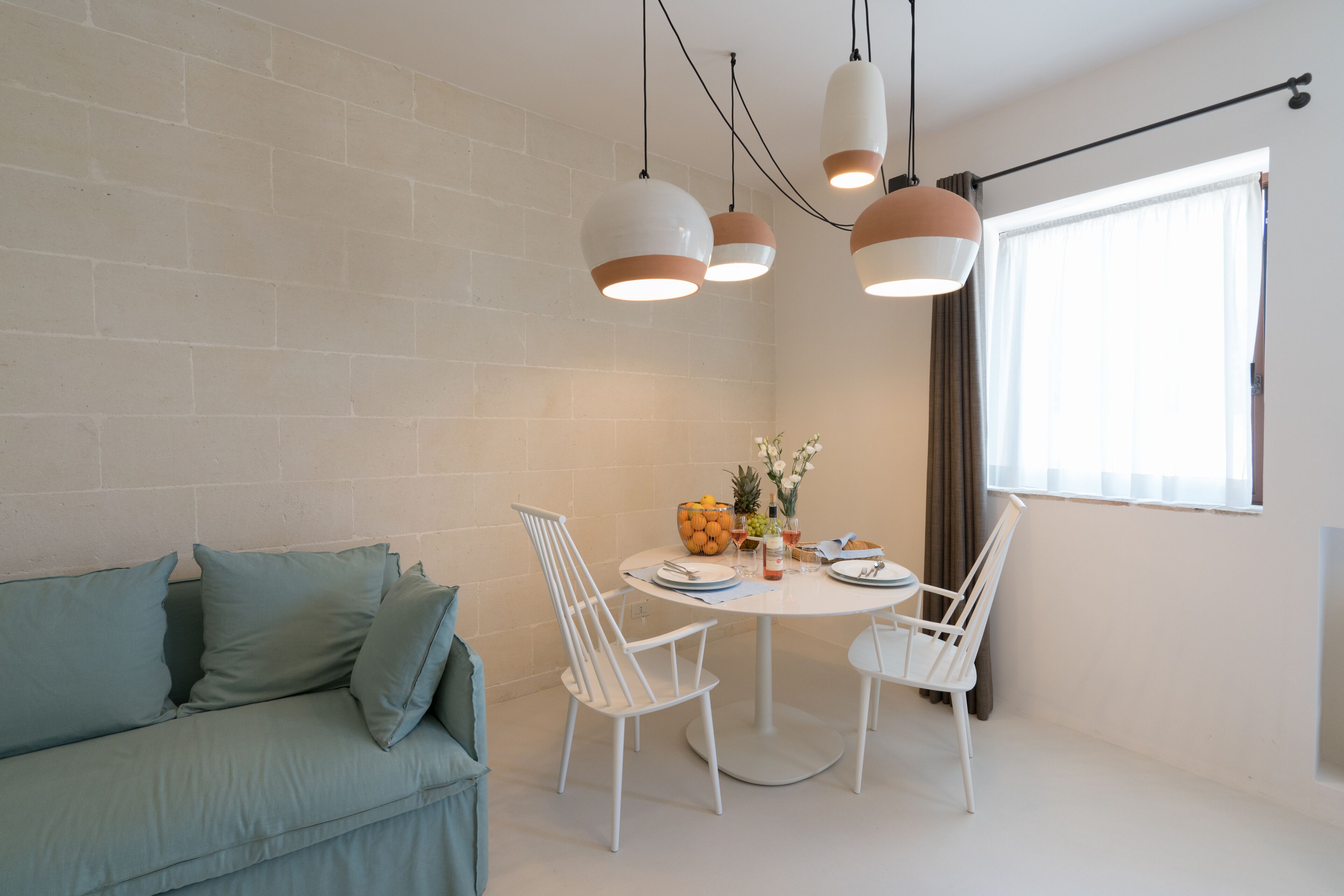 A dining area with a round table, white chairs, and hanging pendant lights.