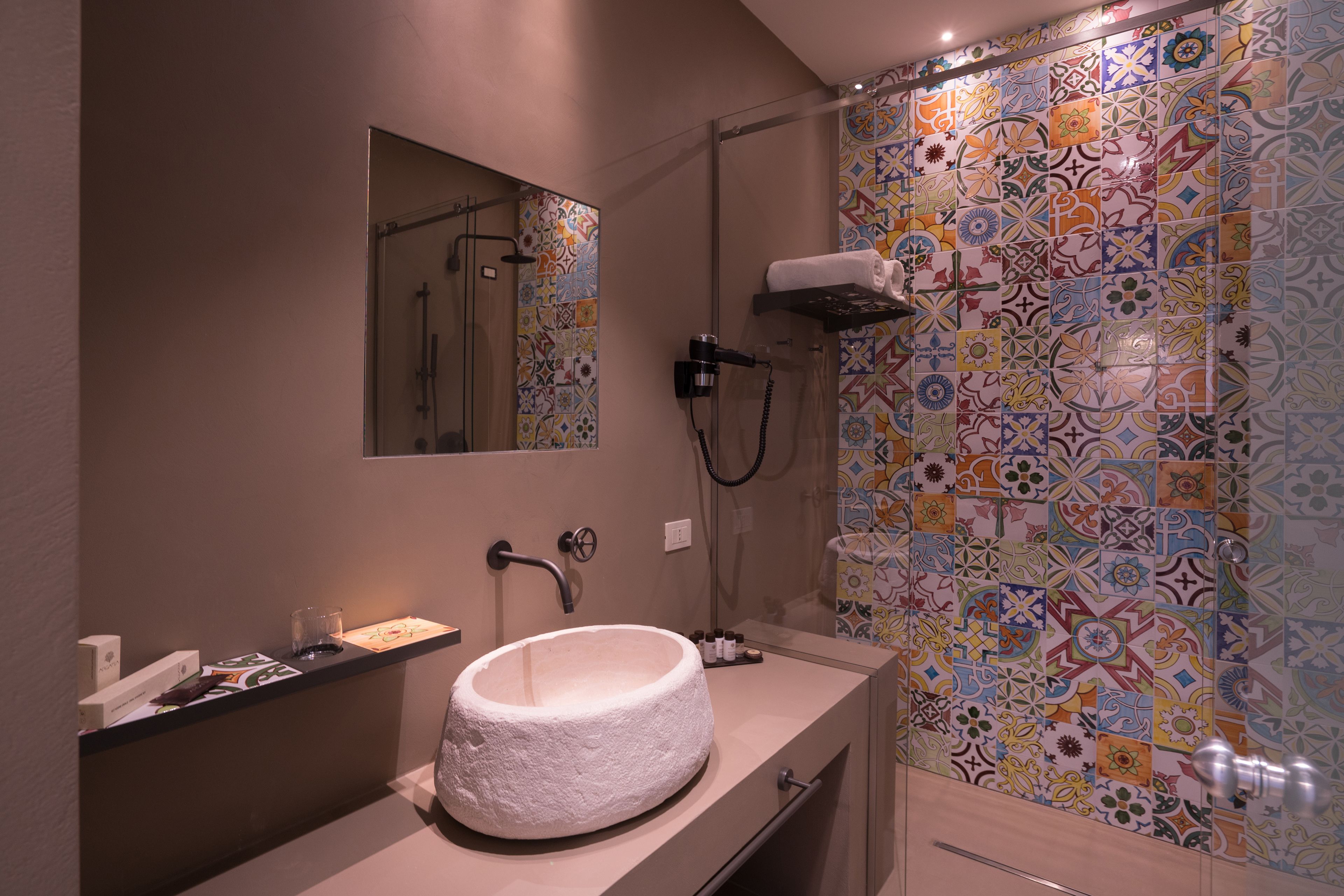 Un baño con un lavabo redondo, un espejo, una ducha y una pared de azulejos coloridos.