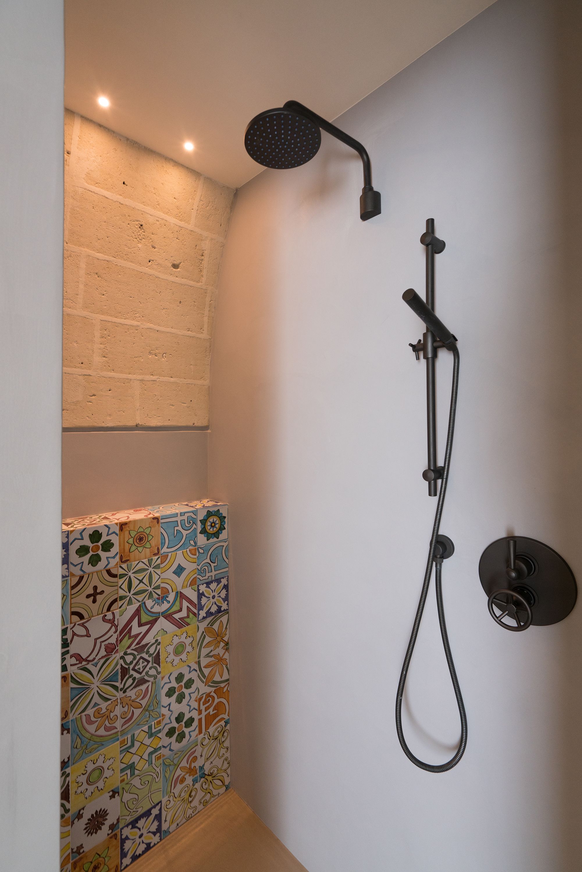 A shower with a handheld showerhead and a wall-mounted control.