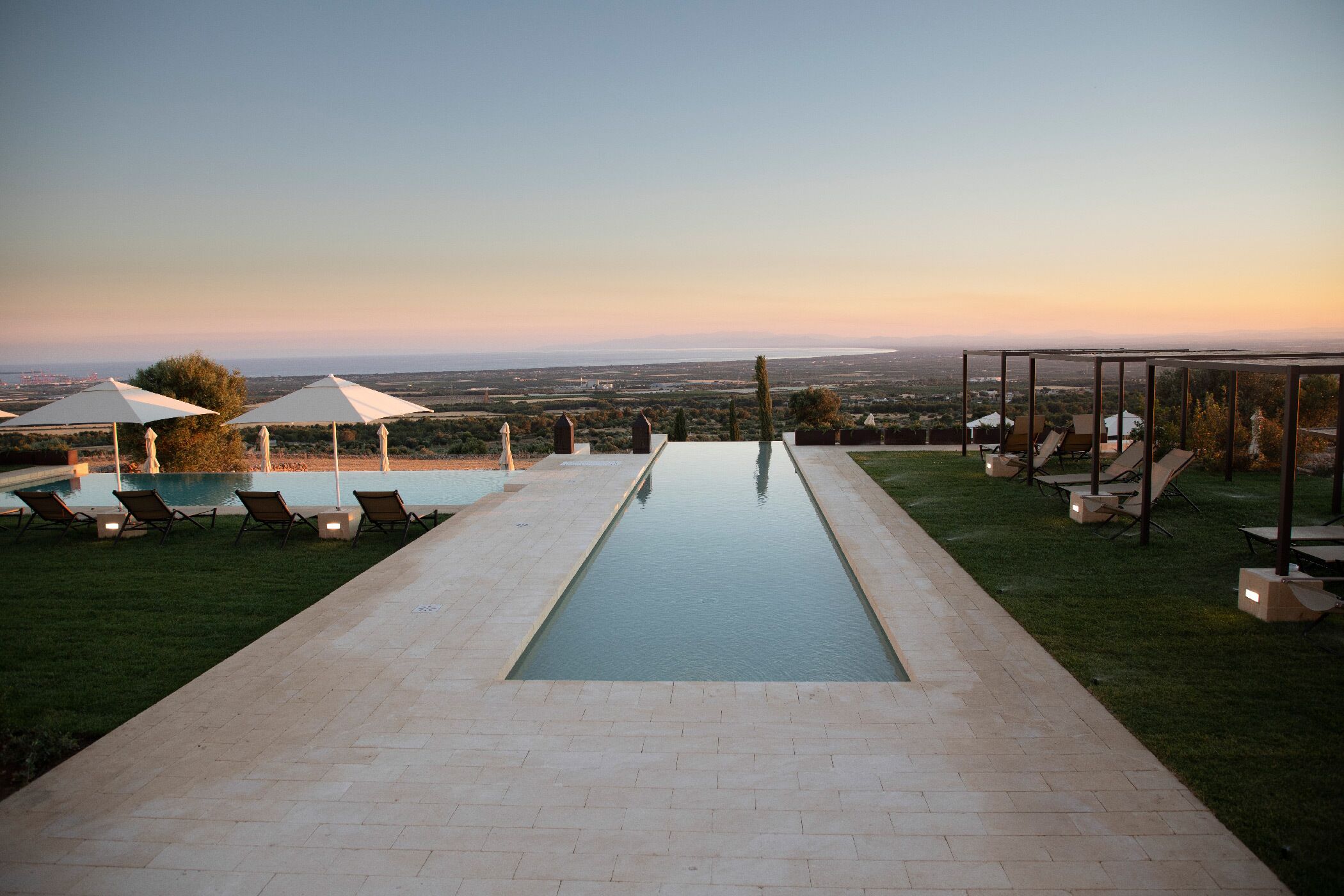 Una piscina con sillones de descanso y sombrillas, rodeada de un césped cuidado y vistas al paisaje.