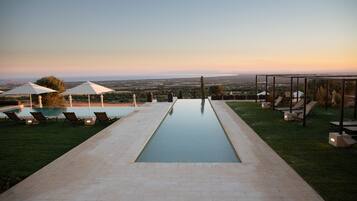 Una piscina con sillones de descanso y sombrillas, rodeada de un césped cuidado y vistas al paisaje.