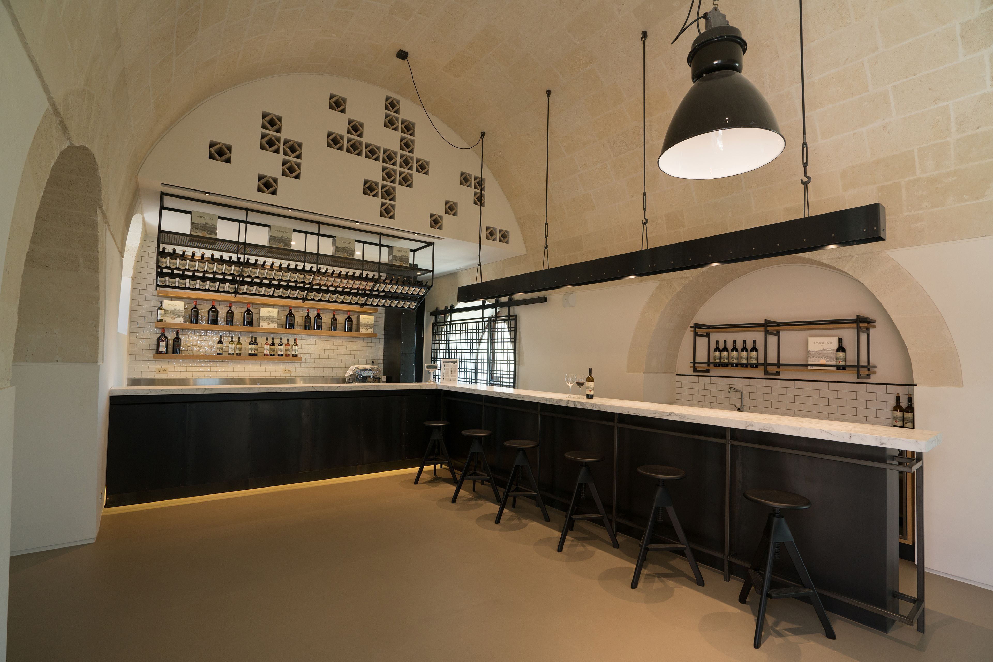 Zona bar con un lungo bancone, diversi sgabelli e una cantina con bottiglie.