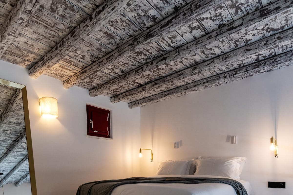 Ein modernes Schlafzimmer mit Holzboden, einem großen Bett mit grauem Kopfteil und Wandleuchten.