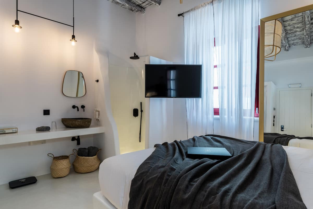 Ein modernes Hotelzimmer mit einem großen Bett, einem Flachbildfernseher, einem Spiegel und einem Ablagefach mit Pflegeprodukten.