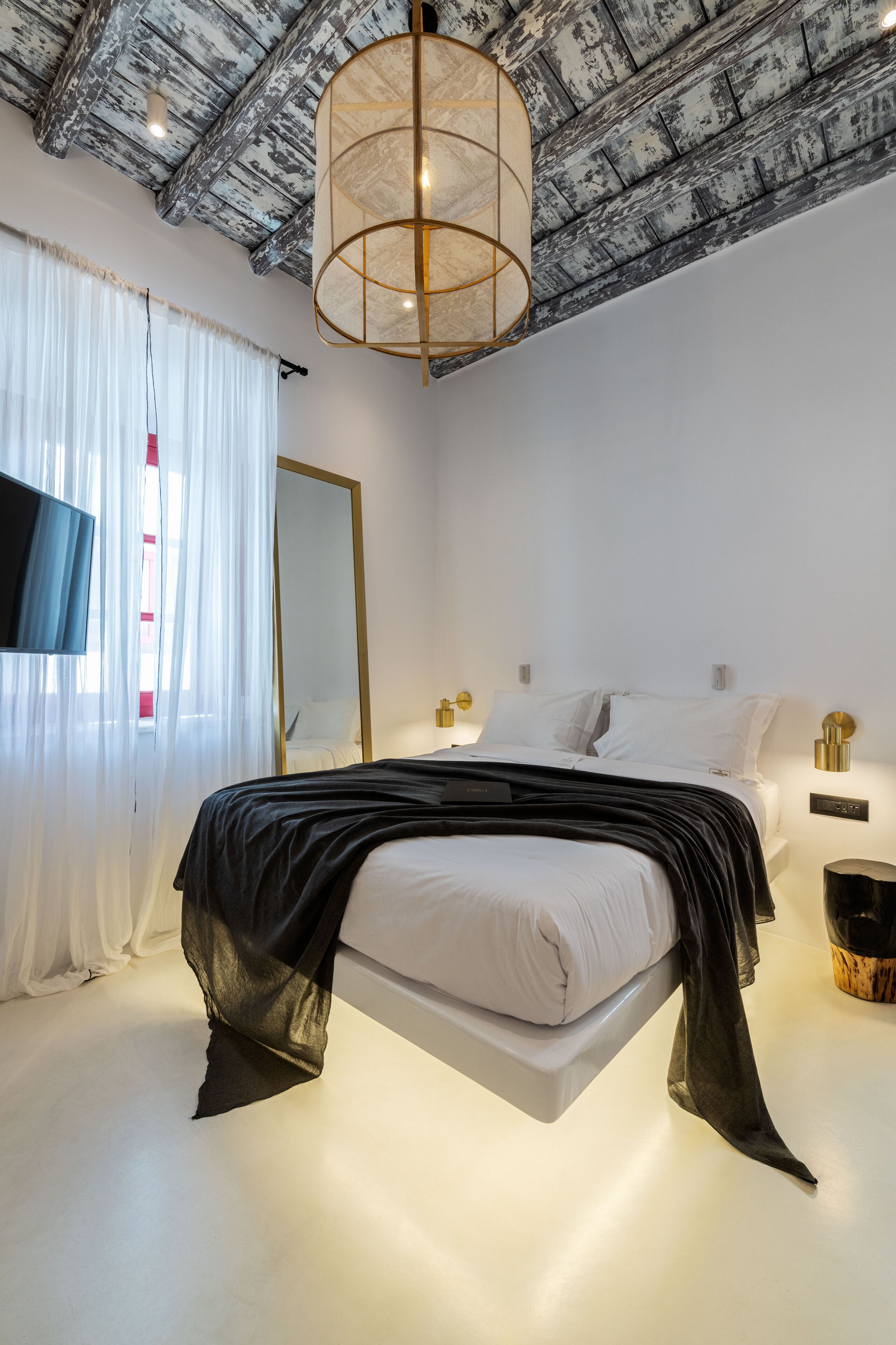 Un dormitorio moderno con una cama suspendida, un espejo grande y un techo con ladrillo visto.