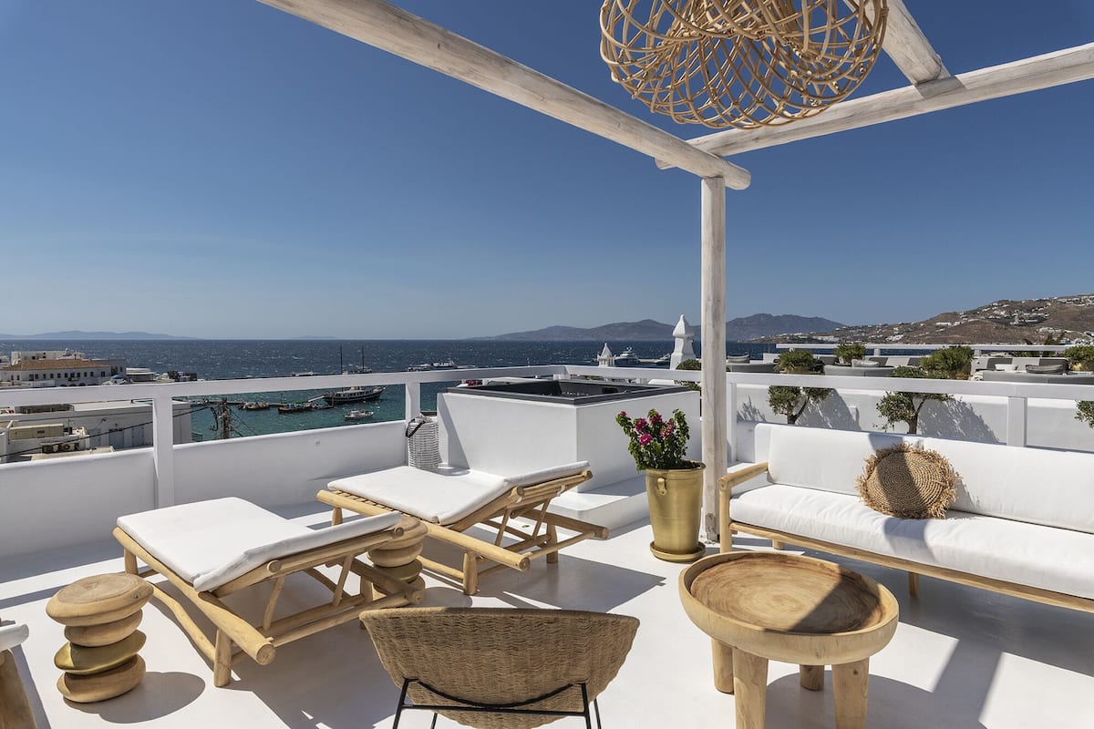 Eine Dachterrasse mit weißer Möbel, Blick auf das Meer und eine gebirgige Landschaft im Hintergrund.