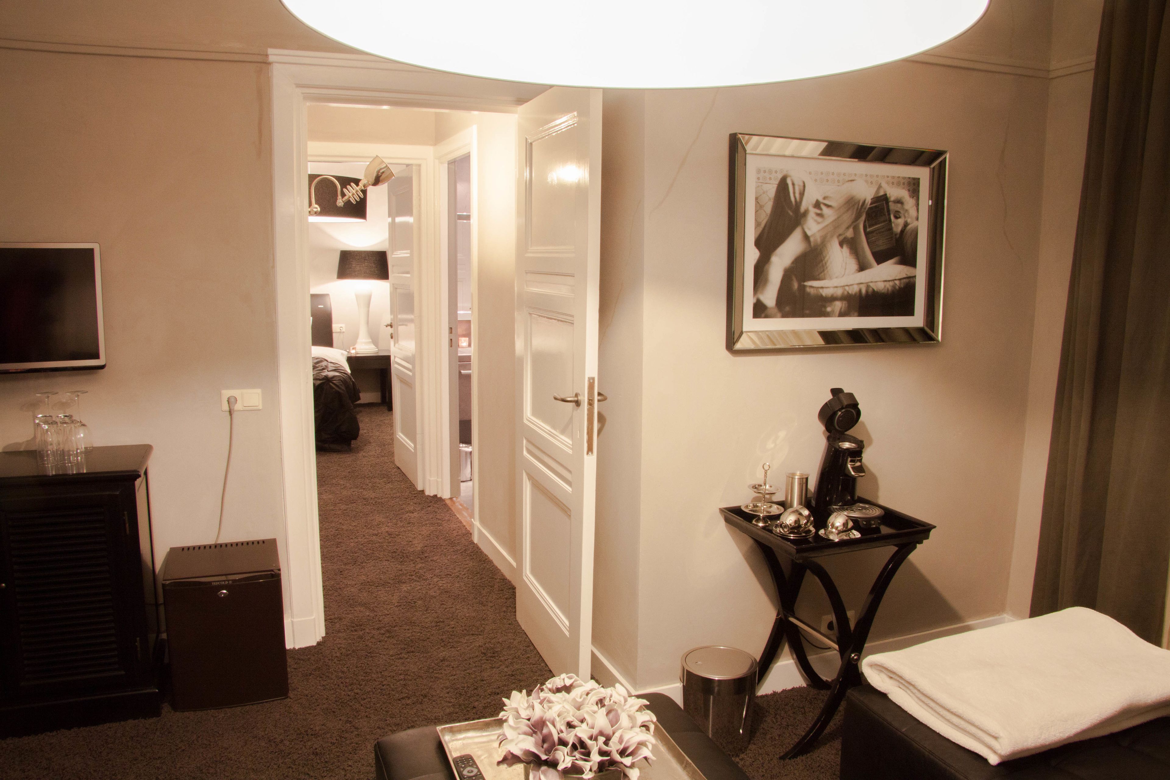 A hotel room with a bed, a bedside table with a lamp, a framed picture on the wall, and a television on the wall.