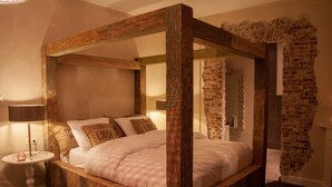 A four-poster bed with a wooden frame and a brick wall backdrop. - Hotel Huis van Bewaring (Almelo)