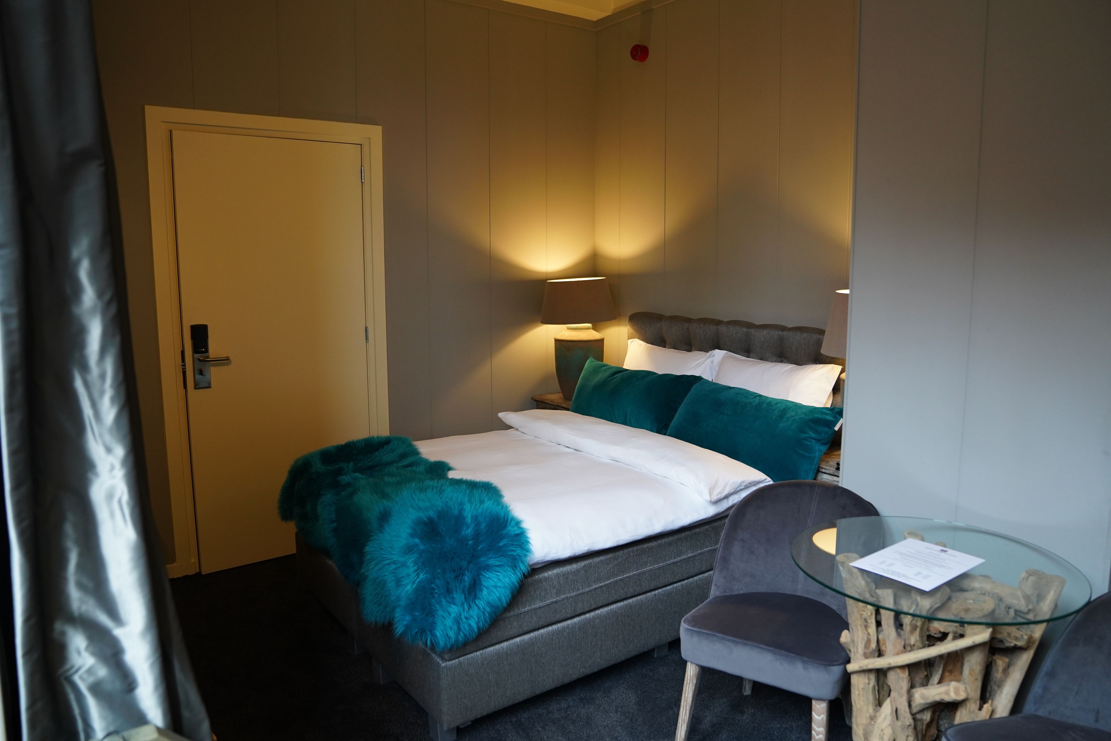 Une chambre d’hôtel avec un lit, une chaise, une table en verre et une lampe.