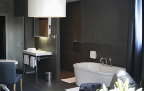A modern bathroom with a white bathtub, a sink, and a mirror. There is a towel rack, a trash bin, and a chair. - Hotel Huis van Bewaring (Almelo)