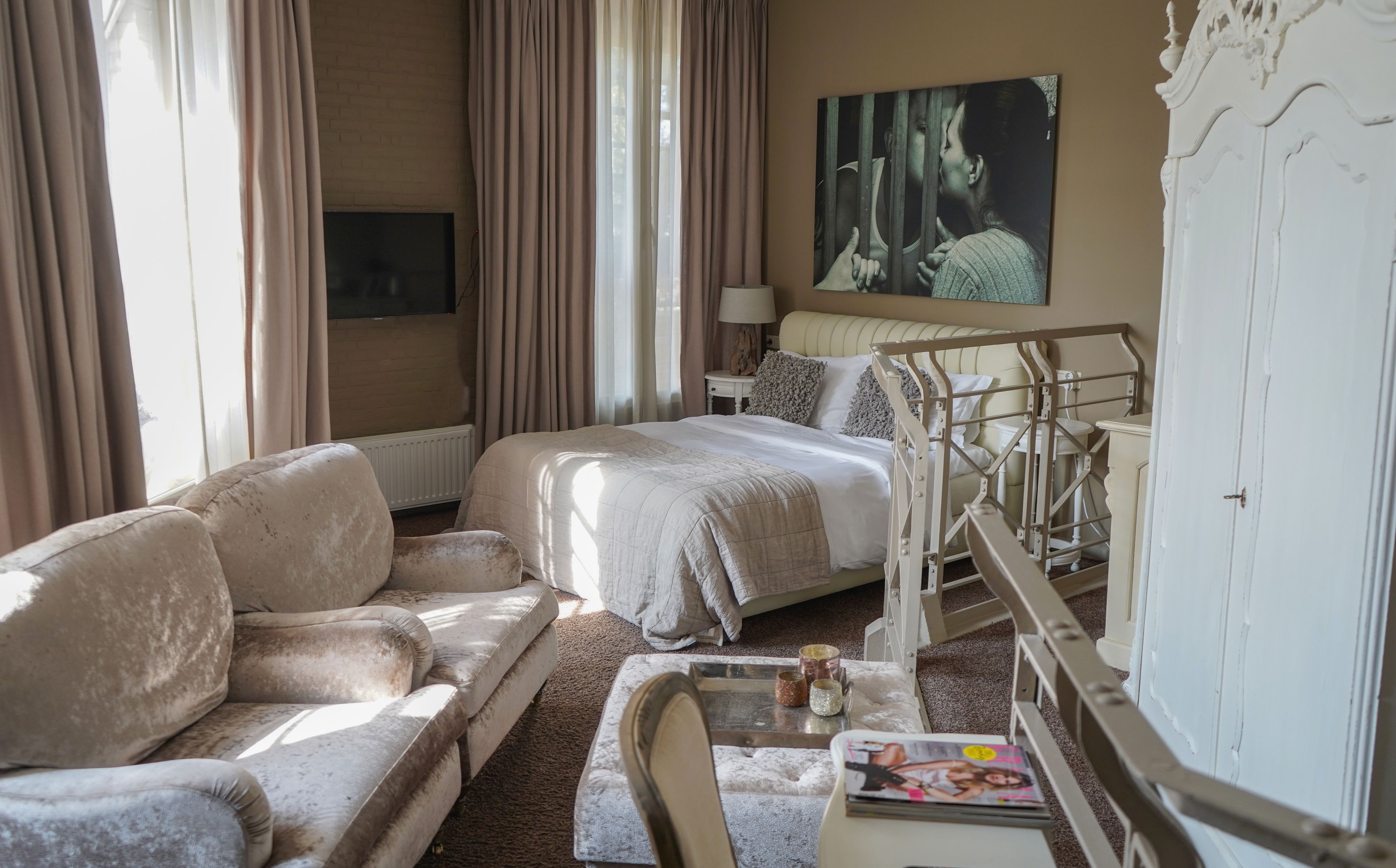 Une chambre d’hôtel avec un lit, un canapé, une petite table avec des magazines, une lampe et un tableau au mur.