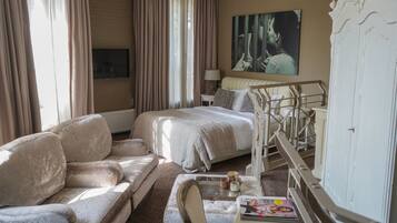 Une chambre d’hôtel avec un lit, un canapé, une petite table avec des magazines, une lampe et un tableau au mur.