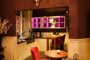 A modern kitchen with white cabinets, a wooden dining table, and red chairs. - Hotel Huis van Bewaring (Almelo)