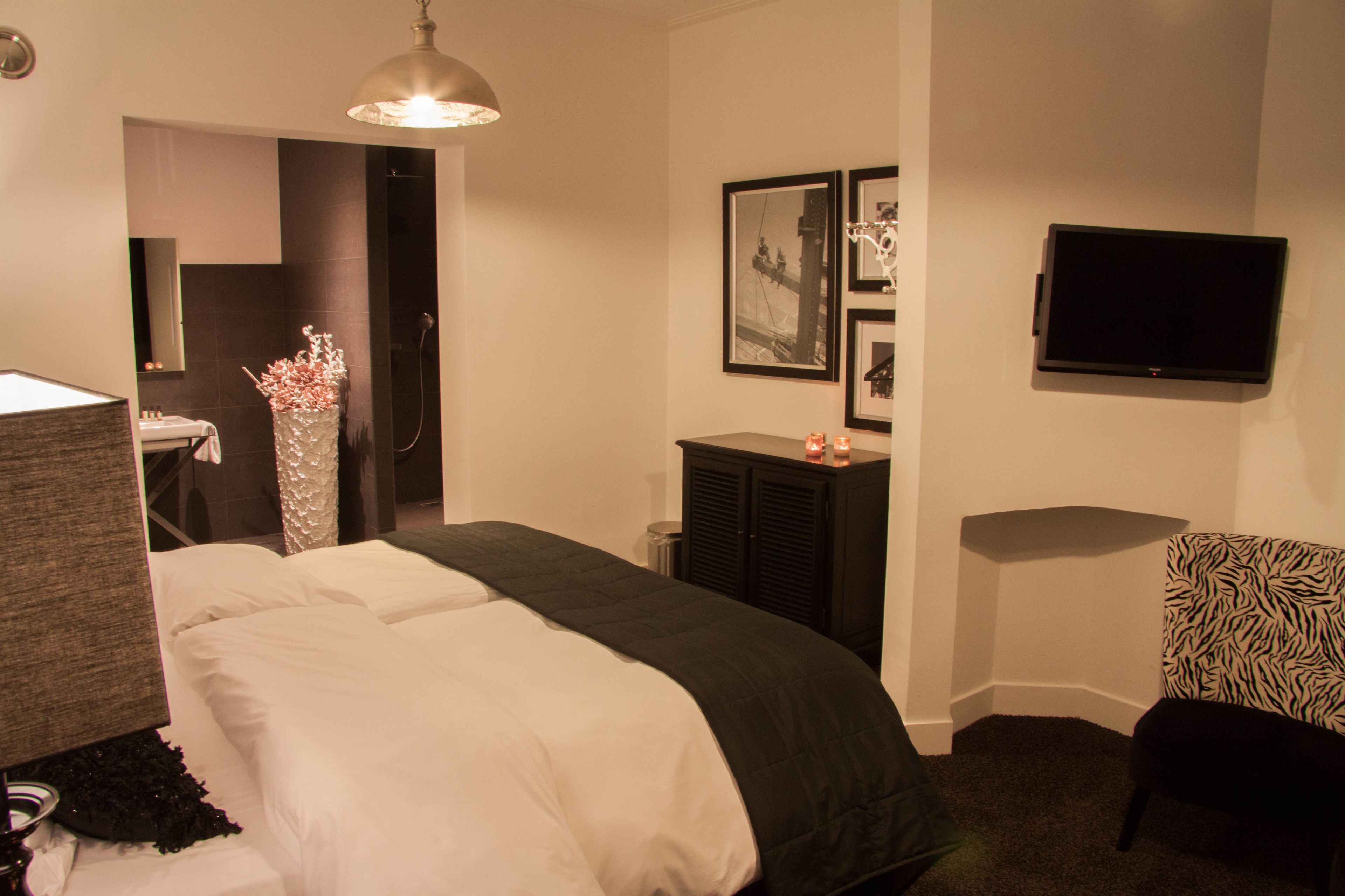 A hotel room with a bed, a desk, a chair, a television, and framed pictures on the wall.