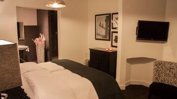 A hotel room with a bed, a desk, a chair, a television, and framed pictures on the wall.