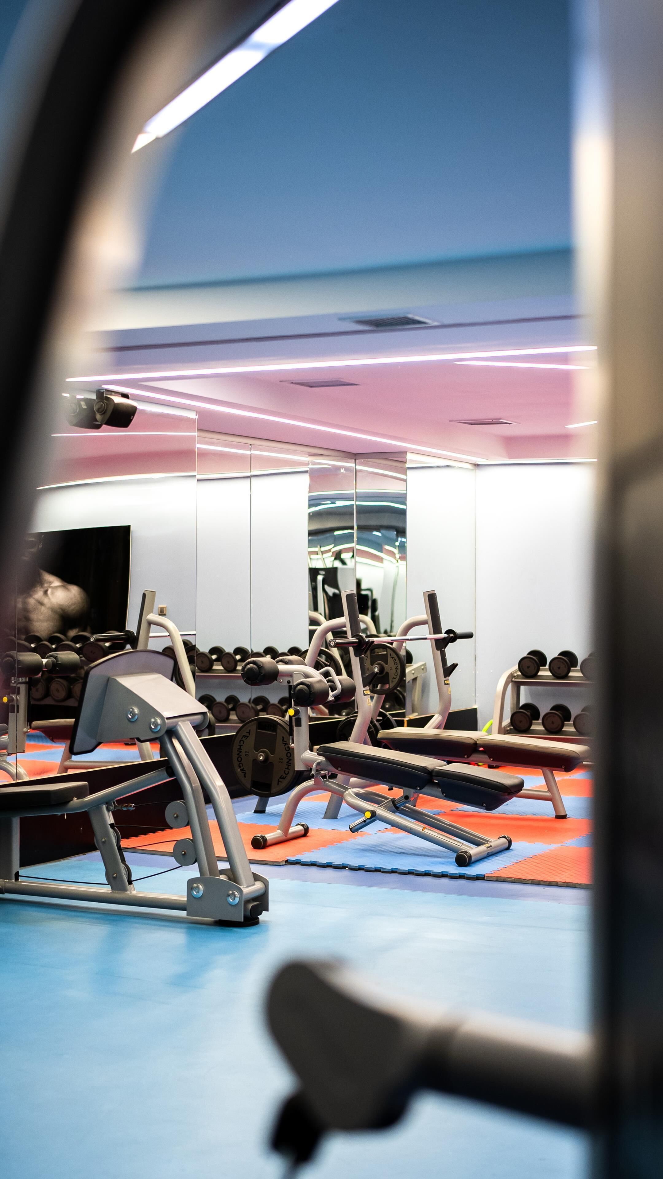 Un gimnasio con equipo de ejercicio, un espejo y suelo azul y rojo.