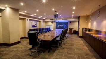 Une salle de conférence équipée d’une longue table, de chaises, d’un pupitre et d’un écran affichant le logo « Radisson Blu ».