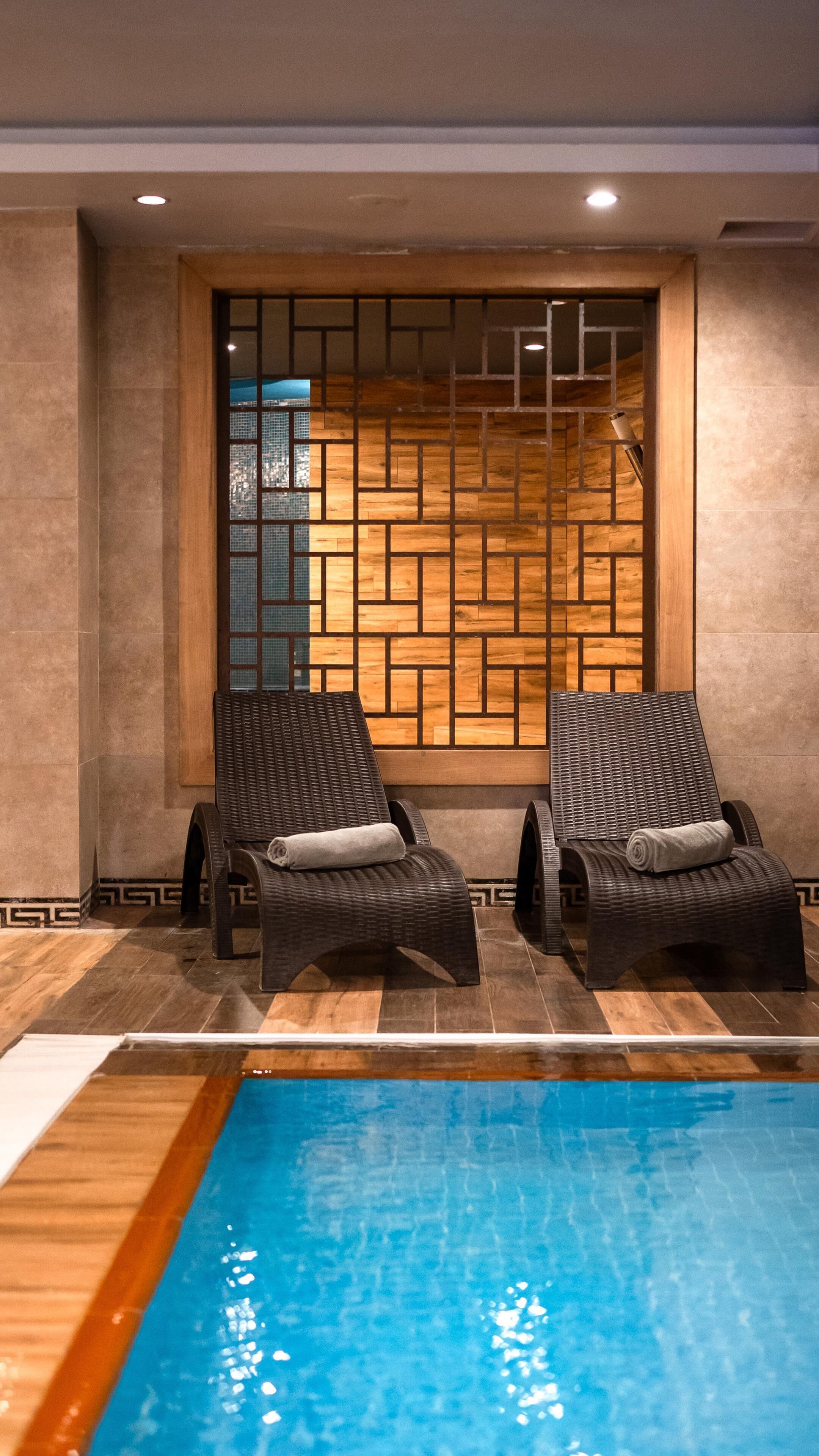 A pool area with two lounge chairs and a wooden wall with a geometric pattern.