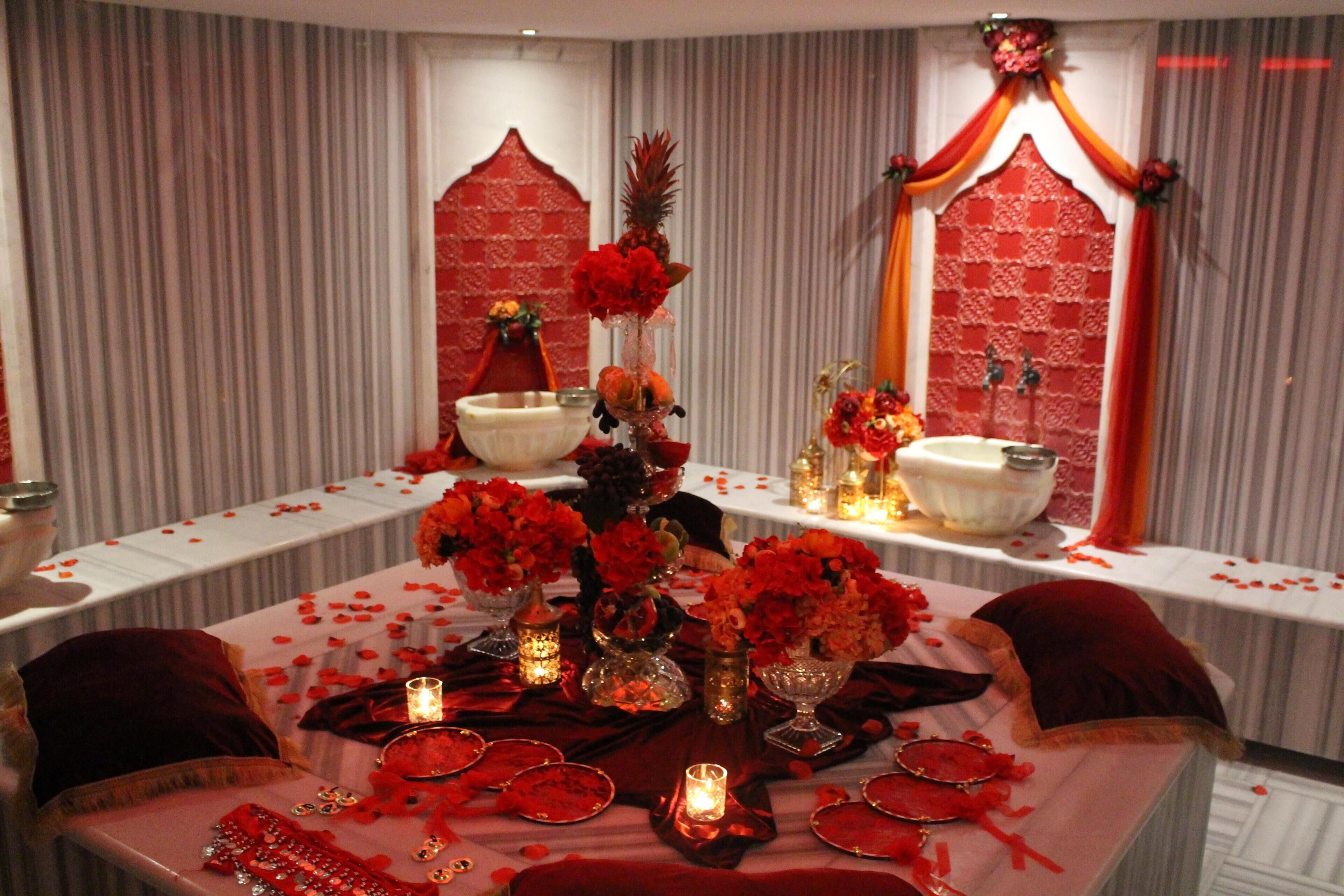 Une table dressée avec des fleurs rouges, des bougies et une nappe rouge, dans une pièce dont le papier peint est à rayures et qui est agrémentée d’une arche décorative.