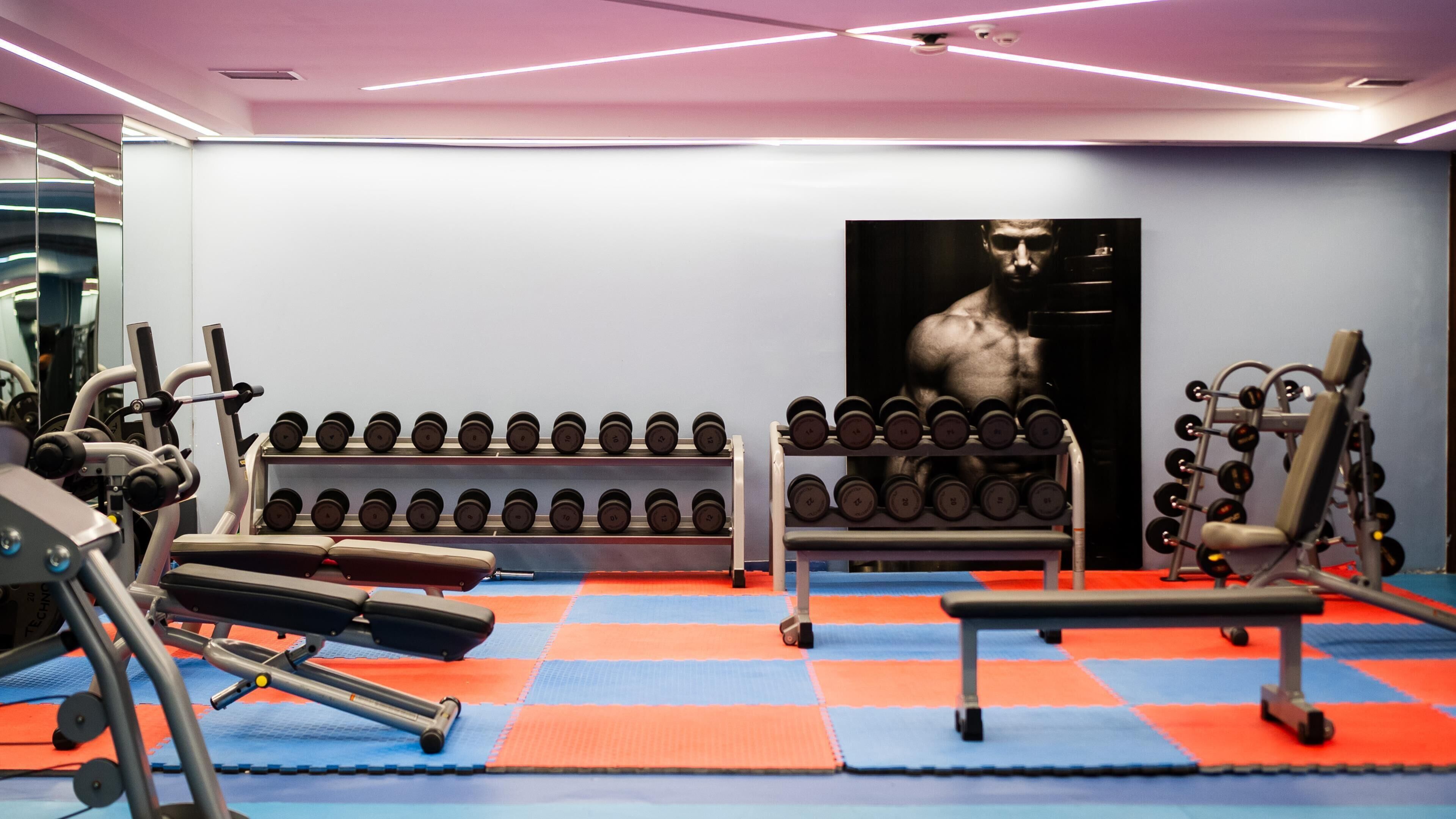 Een sportschool met fitnessapparatuur, een spiegel aan de muur en een poster.