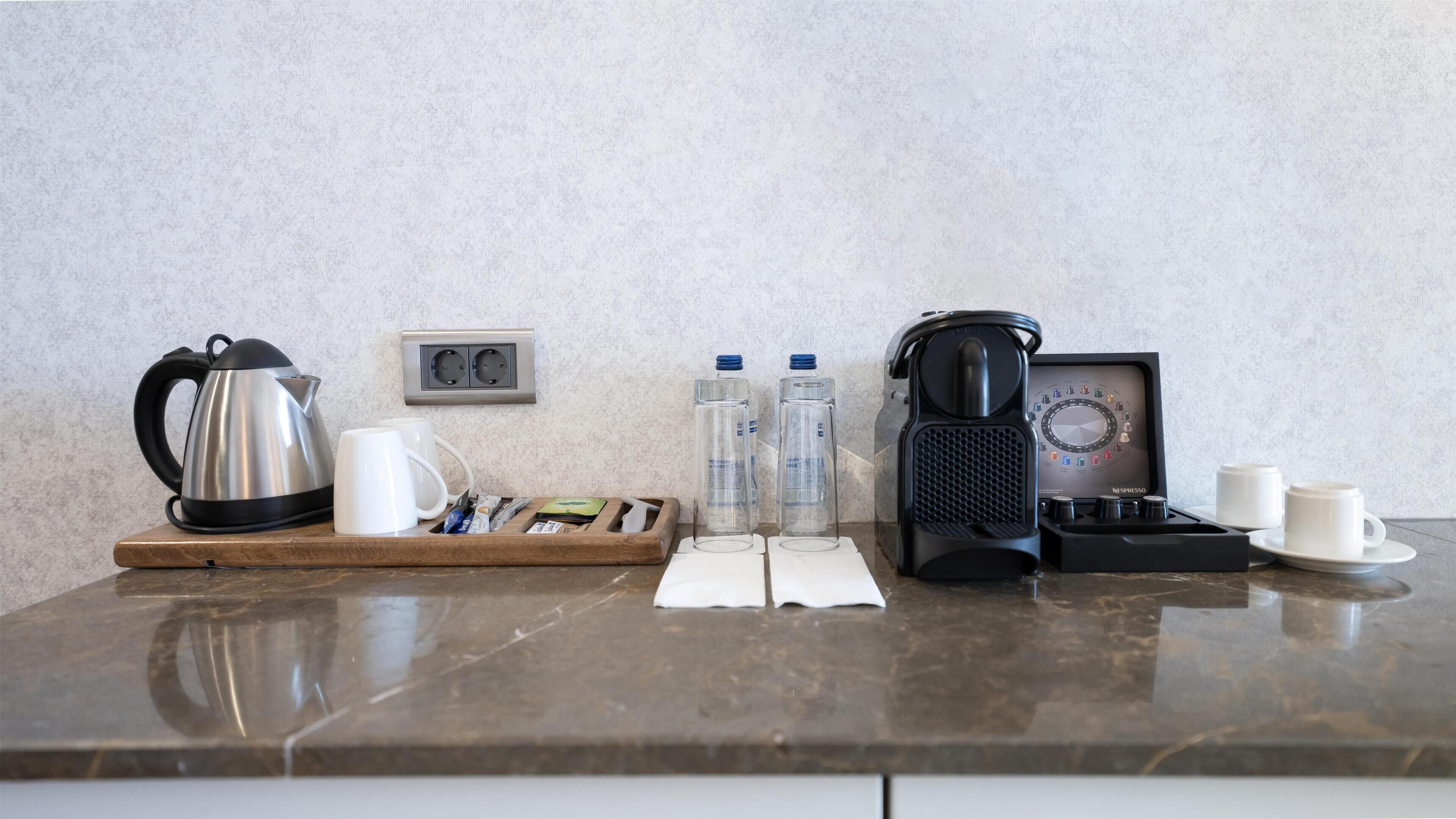 Een keukentafel met een waterkoker, koffiezetapparaat, waterflesjes, koffiekopjes en een dienblad met koffiepads.