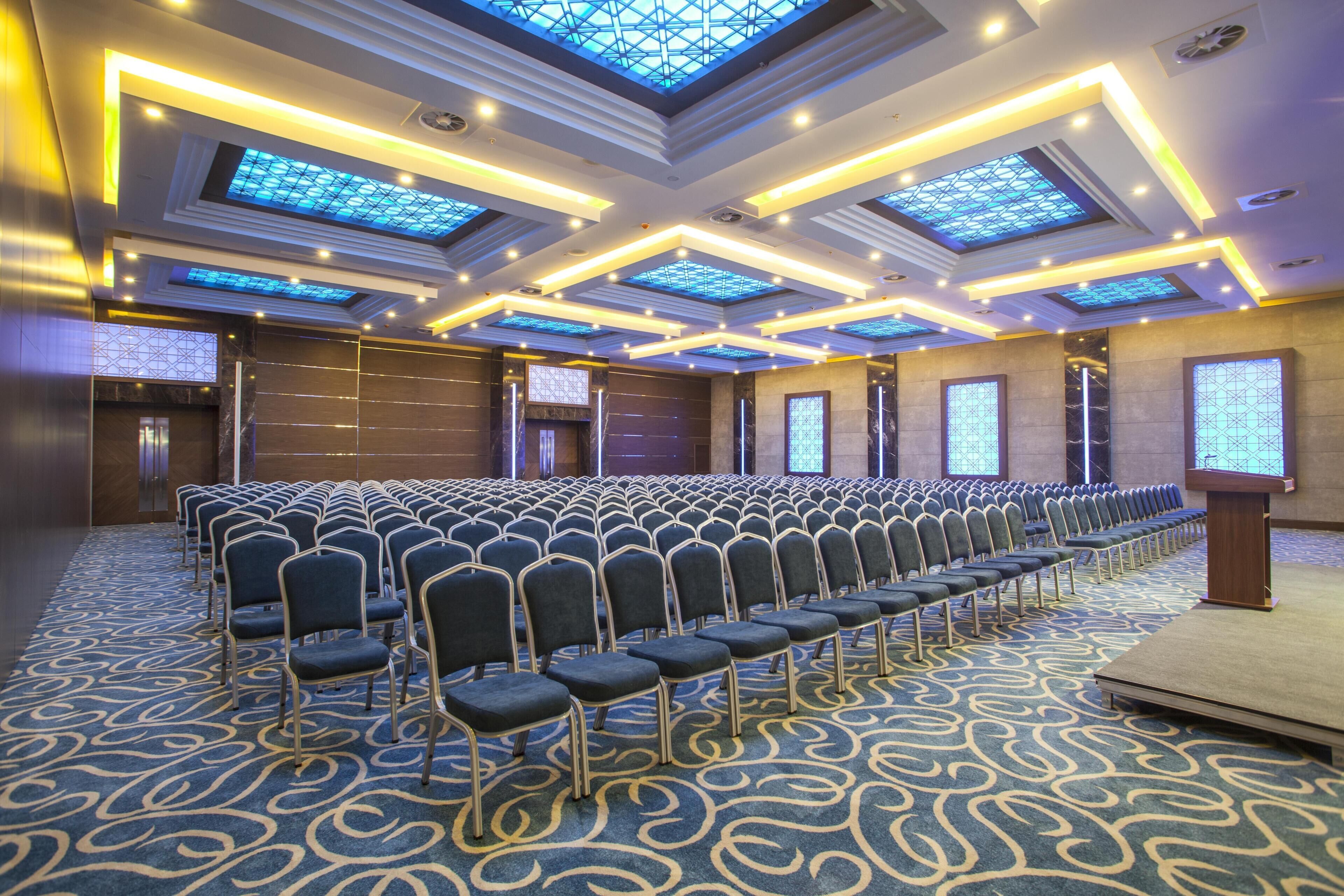 Un salón de conferencias con filas de sillas, un atril y una alfombra estampada.