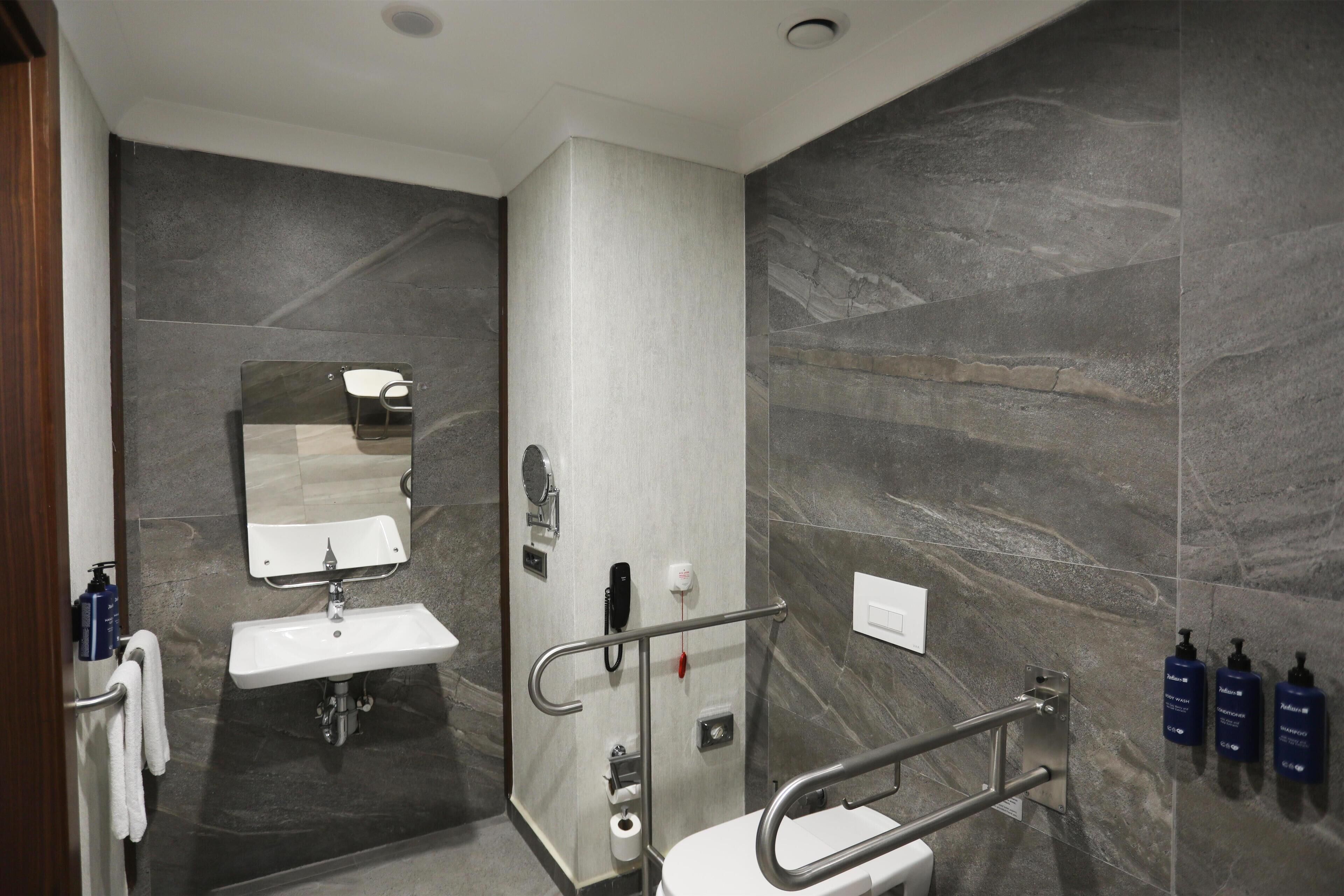 Un baño moderno con lavamanos, espejo, inodoro y barras de apoyo.