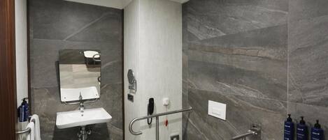 Un baño moderno con lavamanos, espejo, inodoro y barras de apoyo.