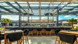 A modern bar area with a glass ceiling, wooden tables, and black chairs. - Royalton Bavaro (Punta Cana)