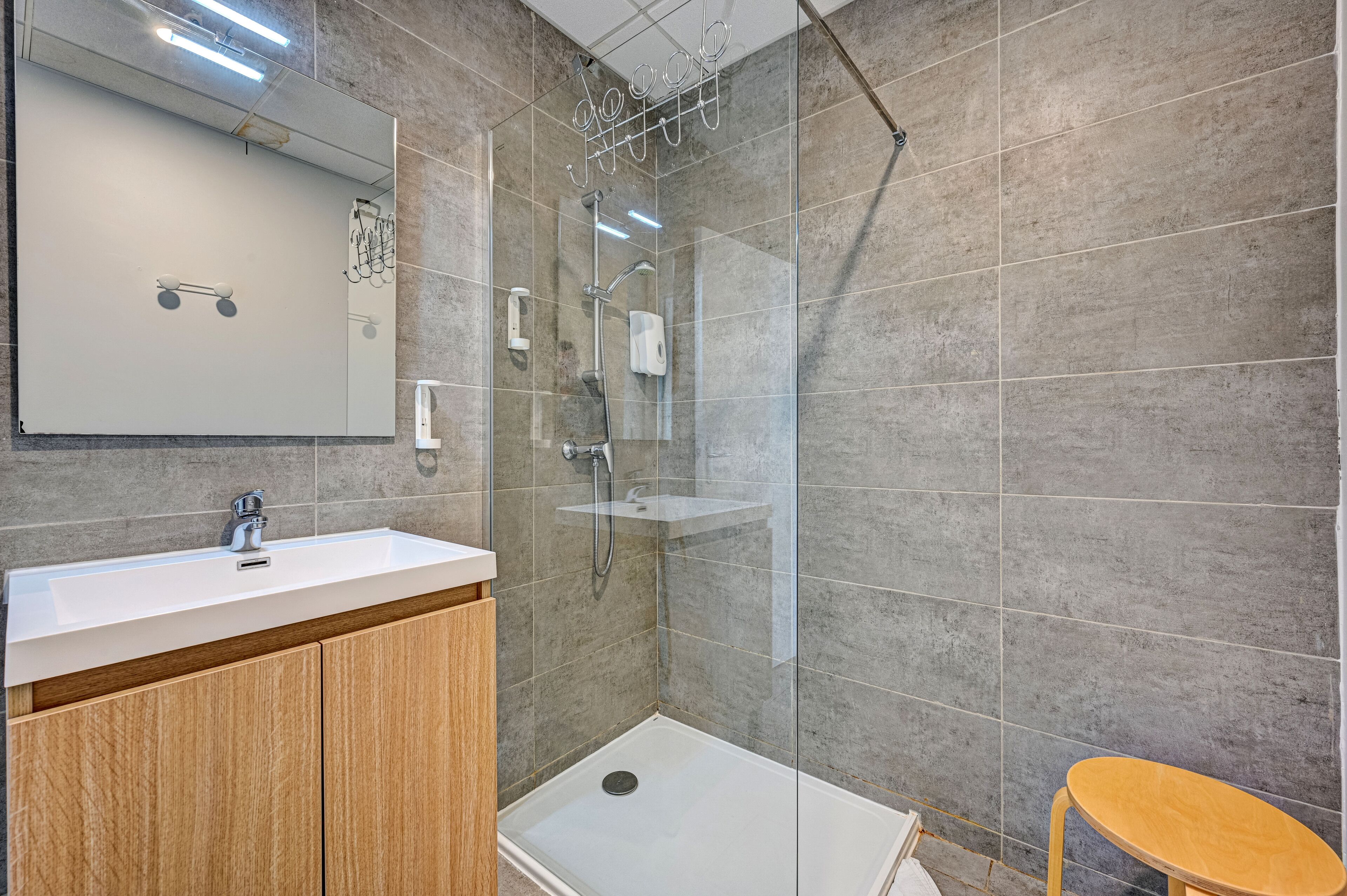 A modern bathroom with a glass-enclosed shower, a white sink, and wooden cabinets.