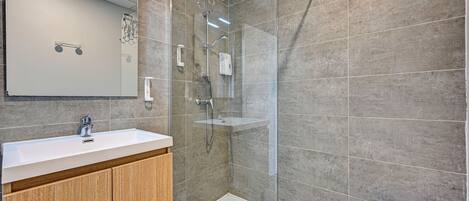 A modern bathroom with a glass-enclosed shower, a white sink, and wooden cabinets.
