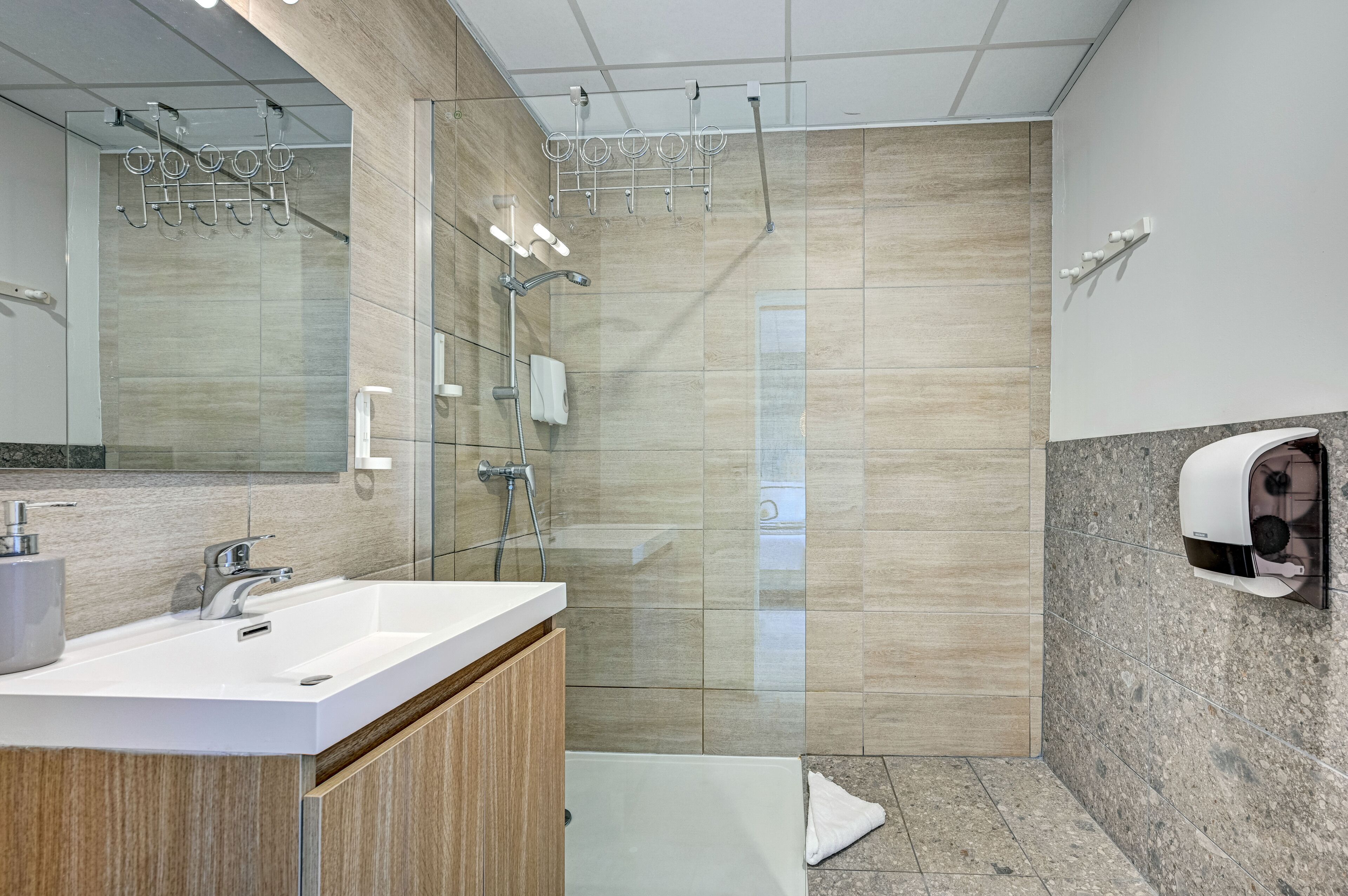 Un baño moderno con un espejo grande, un lavabo con tocador de madera, cabina de ducha de cristal y dispensador de toallas.