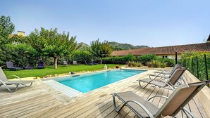 Une piscine rectangulaire dotée d’une terrasse en bois et de chaises longues.