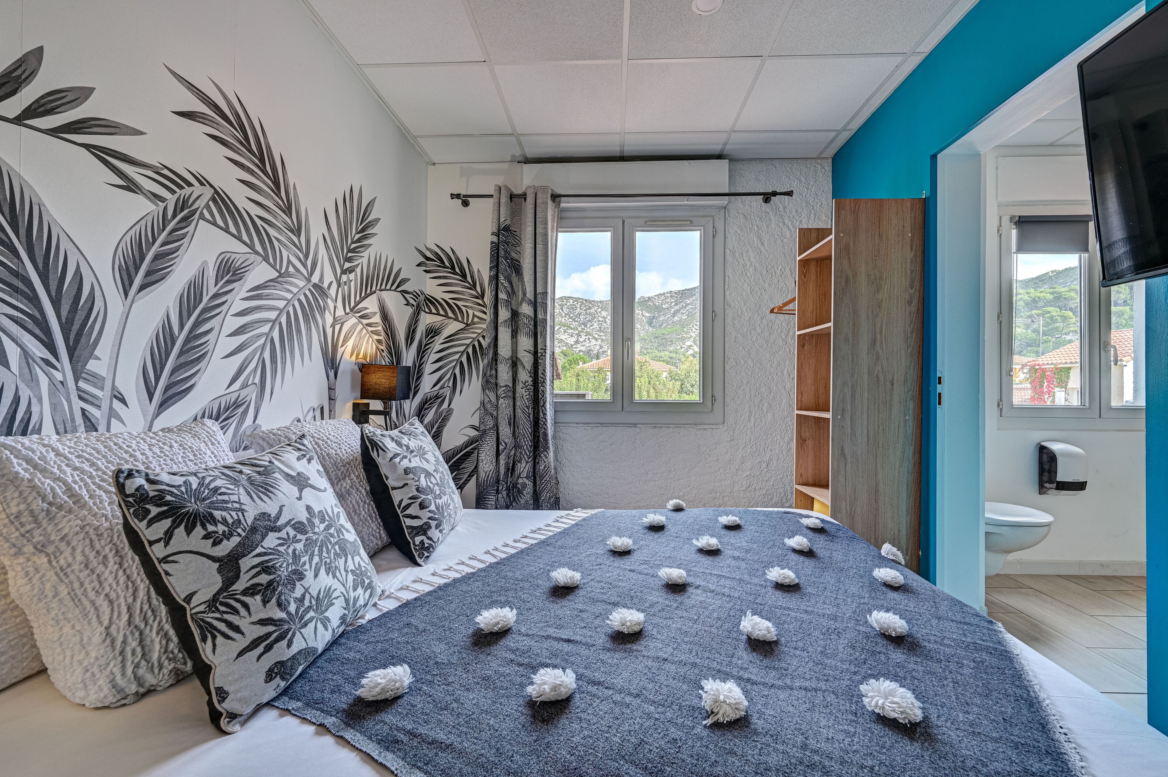 Une chambre à coucher avec un lit, des oreillers, une fenêtre, une salle de bain et une vue sur l’extérieur.