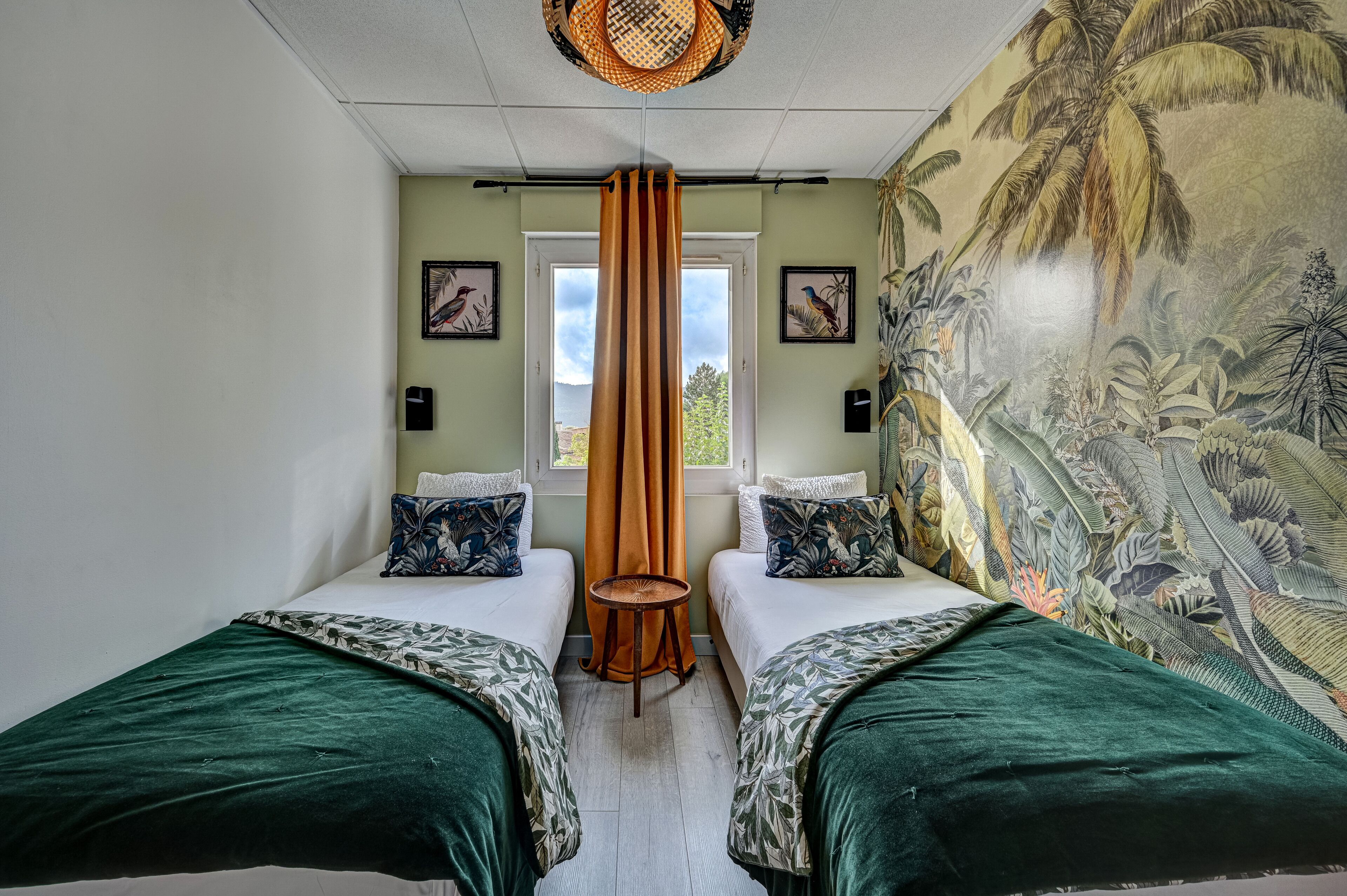 A room with two beds, a window with curtains, and a mural on the wall.