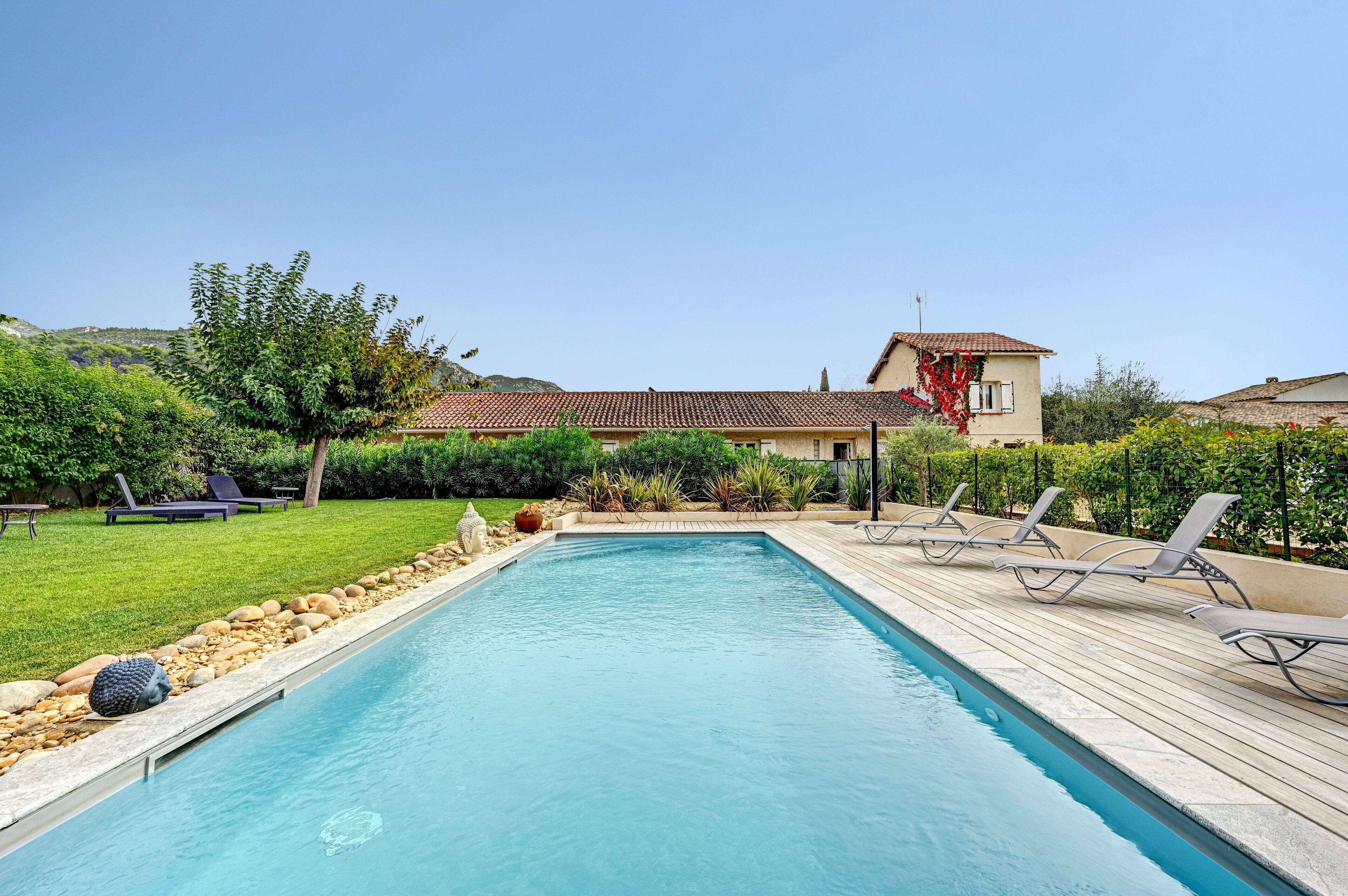 Una piscina rectangular con muelle de madera y sillones de descanso.