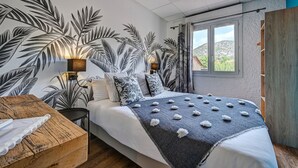Une chambre avec un grand lit, une table de chevet en bois, une lampe fixée au mur et une vue sur l’extérieur par une fenêtre.
