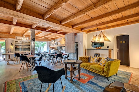 A spacious living area with a wooden ceiling, a yellow sofa, and a dining table with chairs.