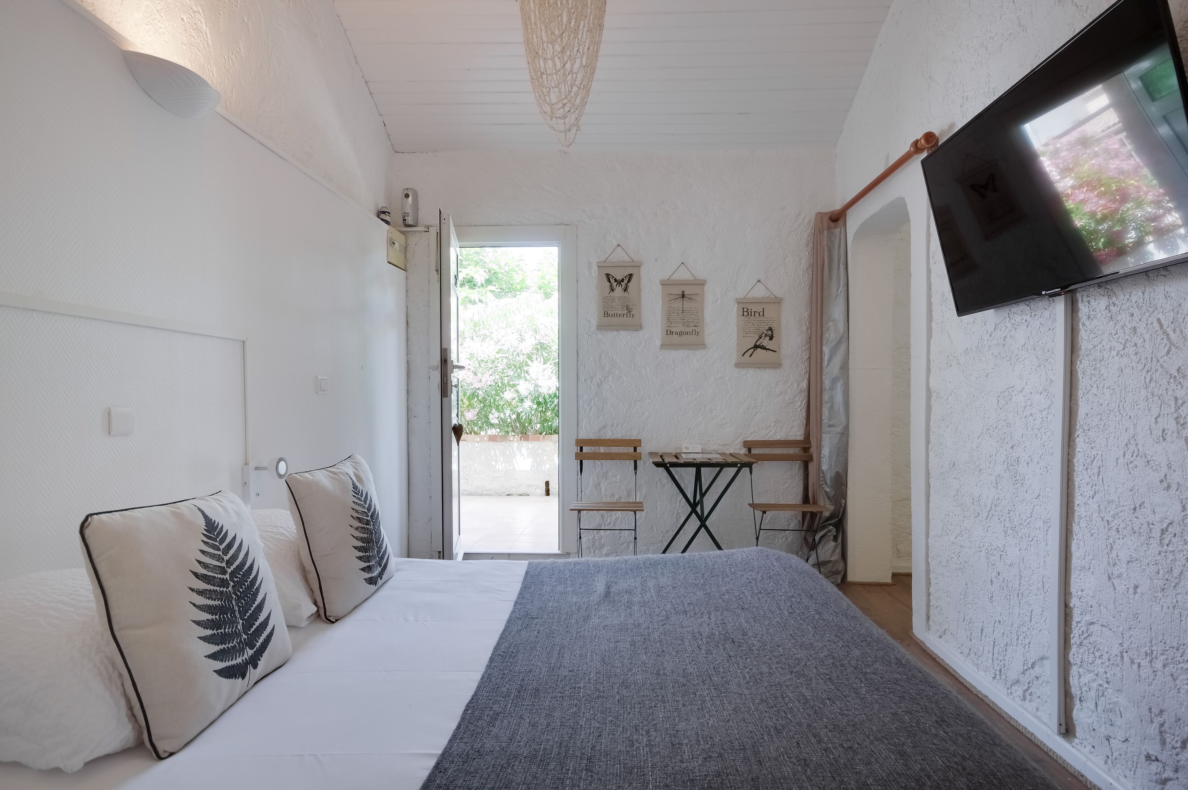 Un dormitorio con cama, dos almohadas, televisor, mesita y sillas.
