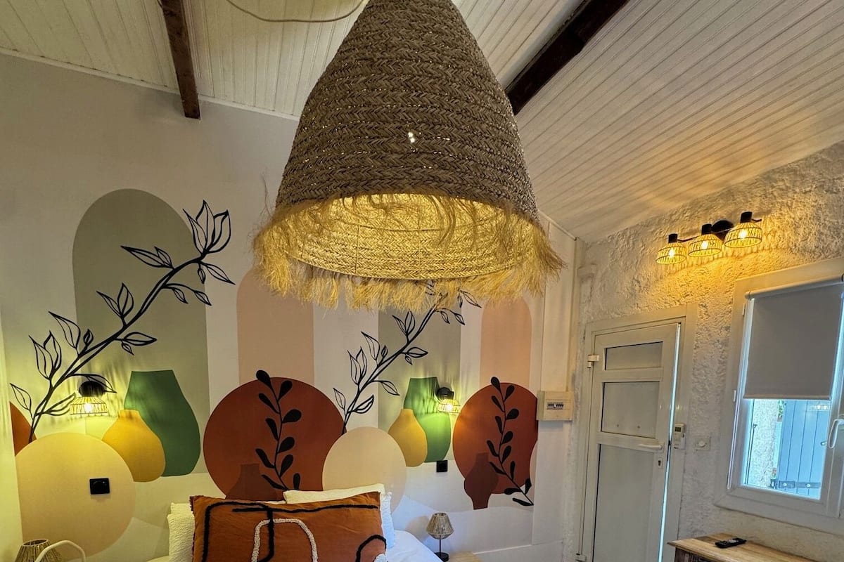 A hotel room with a bed, a hanging lamp, wall art, and a window.