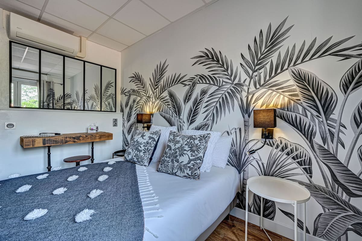 A bedroom with a large bed, a mirror, a nightstand, and a wall with a tropical leaf pattern.