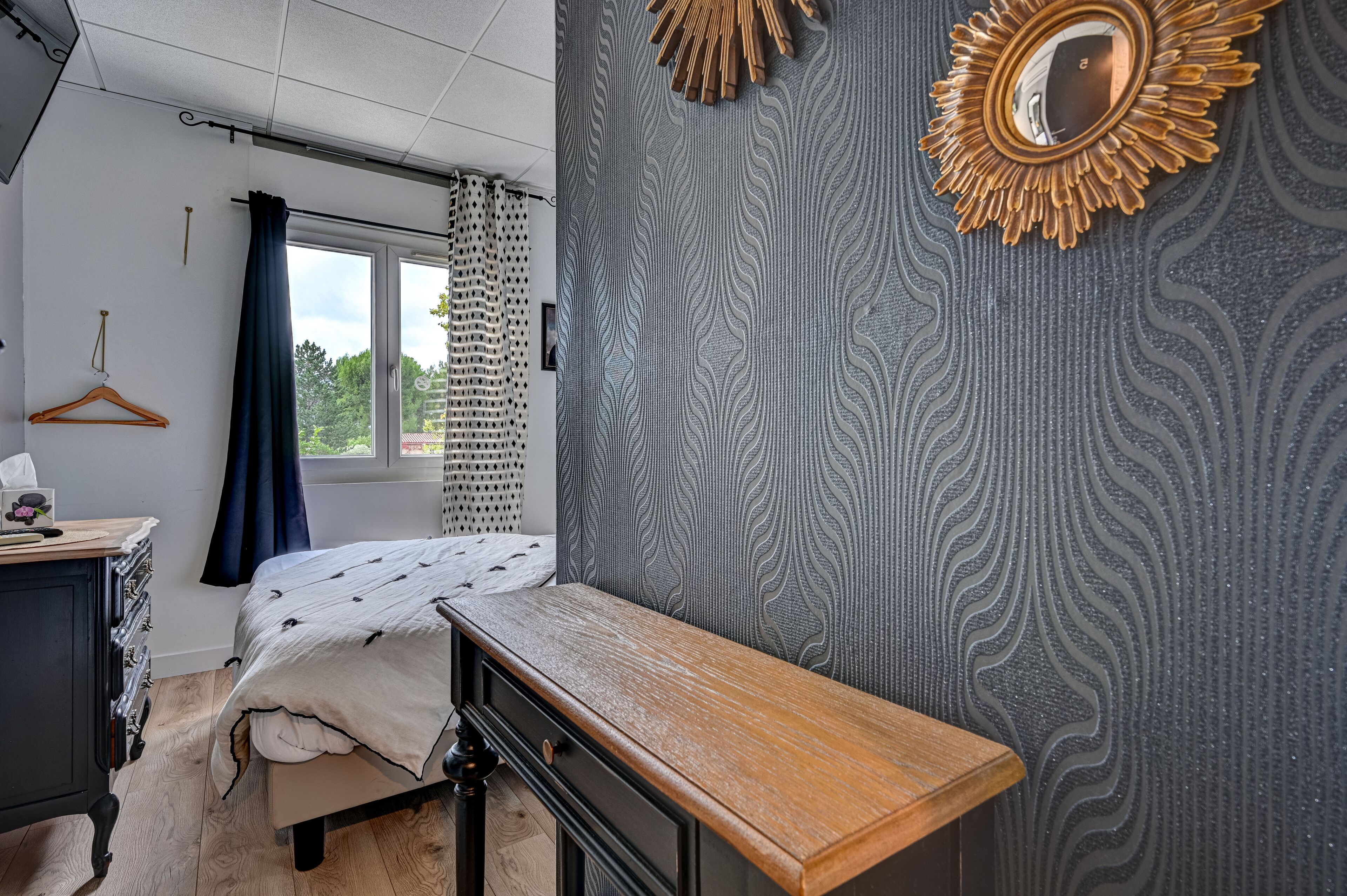 Une chambre à coucher comprenant un lit, une table de chevet, une commode et une fenêtre avec des rideaux.