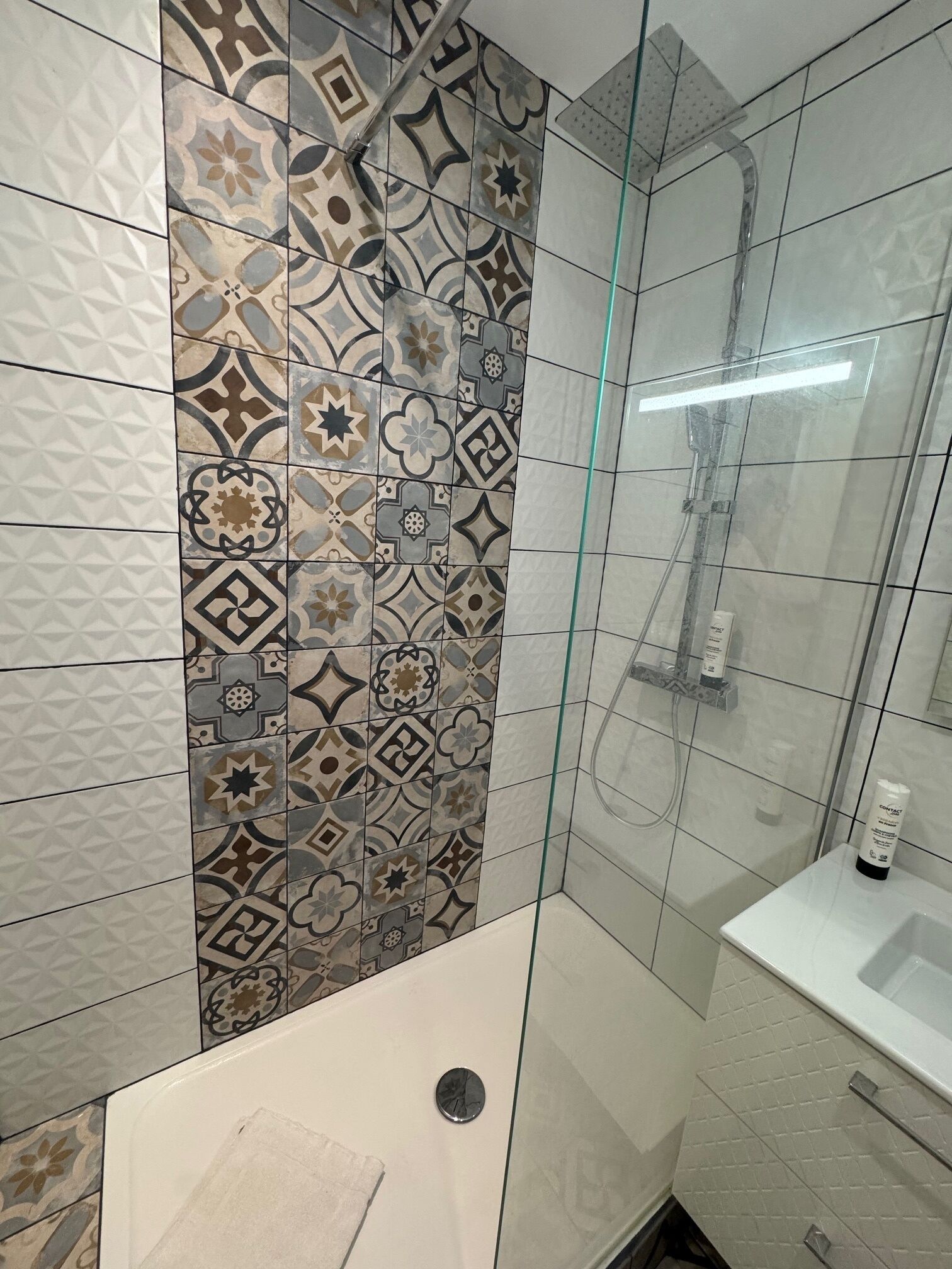 A bathroom with patterned tiles, a glass shower enclosure, and a white sink.