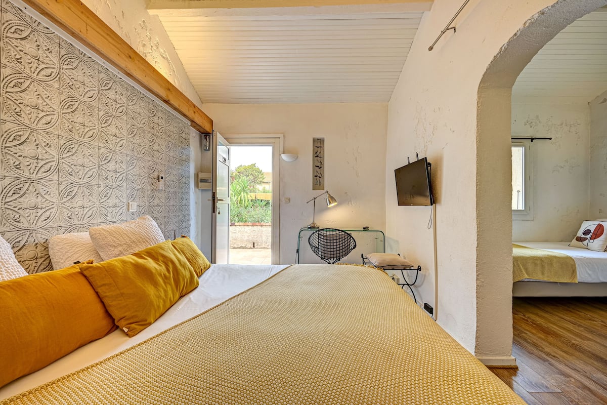 A bedroom with a bed, a desk, and a chair. There is a door leading to an outdoor area.