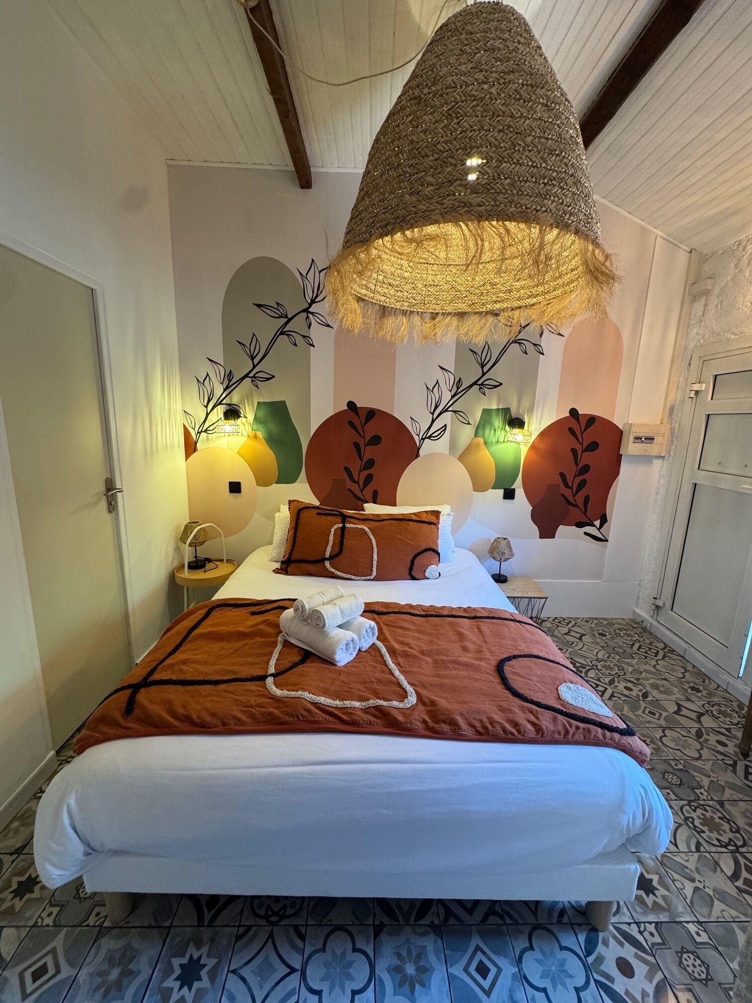 Una habitación de hotel con una cama grande, detalles decorativos en la pared y una lámpara de techo tejida y original.